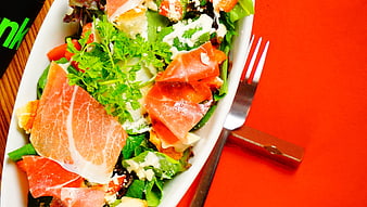 Overhead view of prosciutto salad on white plate with fork