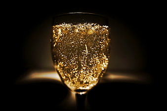 Close-up of sparkling wine glass with golden bubbles in dark setting
