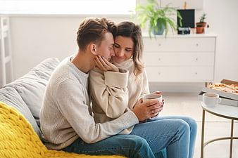 Happy couple cuddling on sofa with coffee and pizza