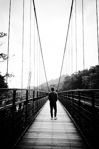 Man Walking on Suspension Bridge in Black and White