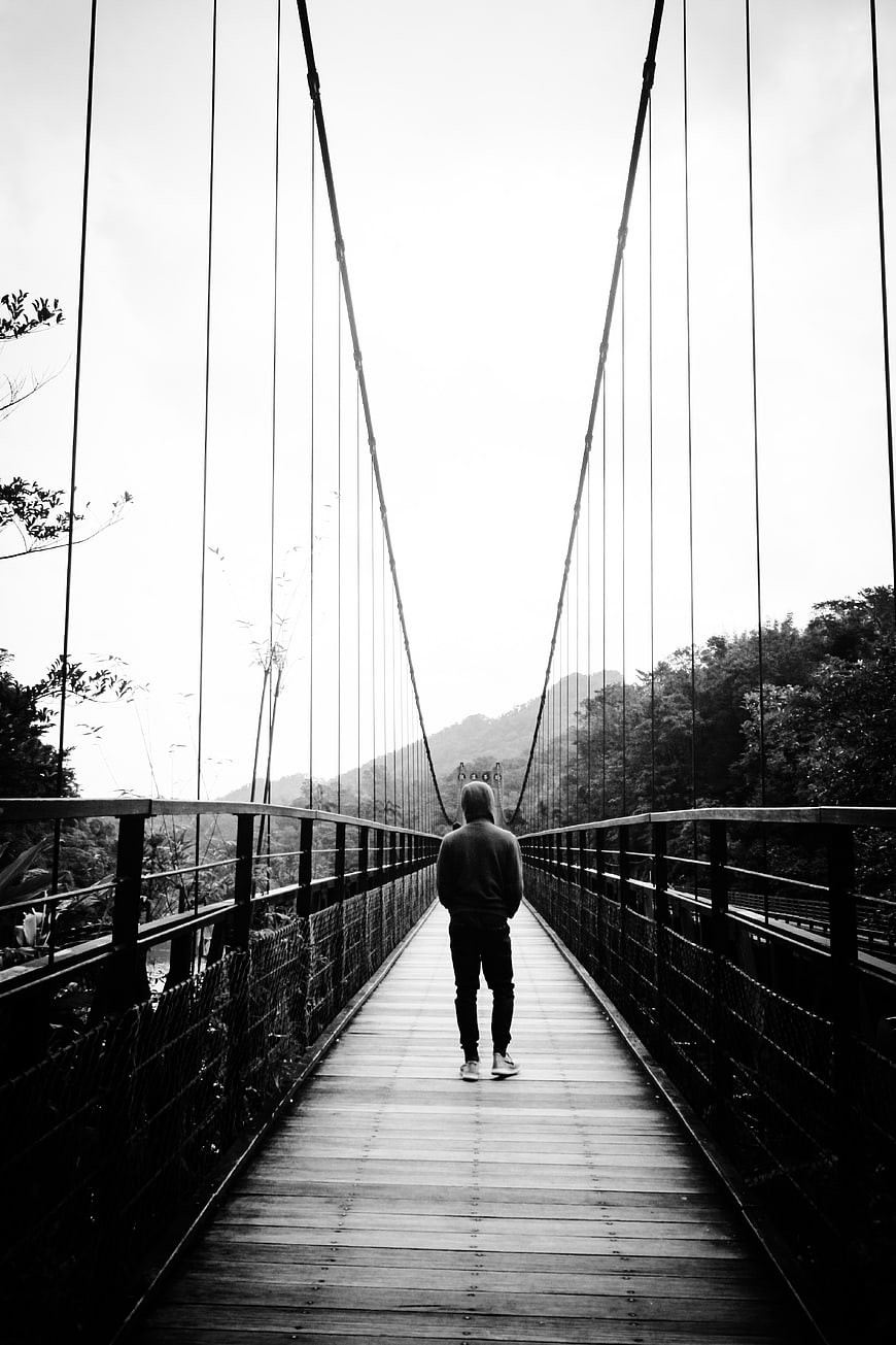 Man Walking on Suspension Bridge in Black and White