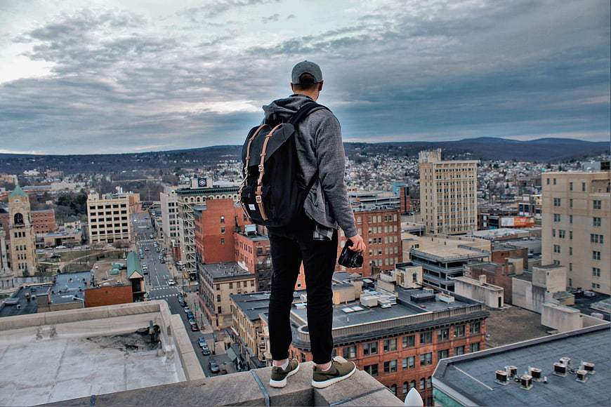 Man with backpack and camera standing on rooftop overlooking city skyline