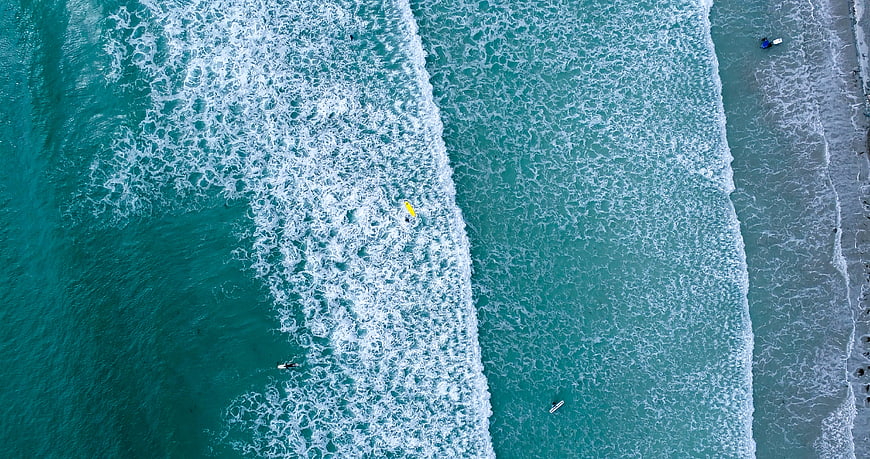 Aerial View of Turquoise Ocean Waves and Surfers