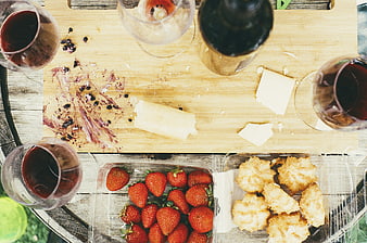 Overhead view of wine, cheese, strawberries, and cookies on a wooden board