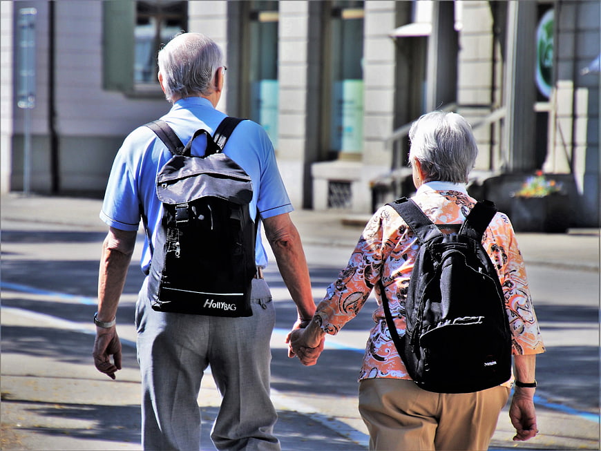 Senior couple walking hand in hand with backpacks