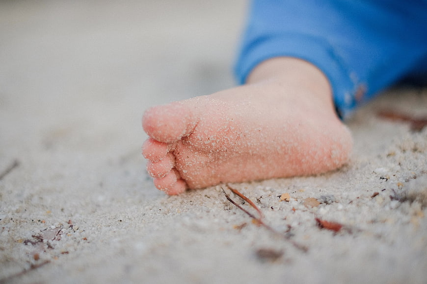 Close-up of baby foot covered in sand on beach