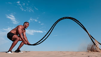 Athletic Man Training with Battle Ropes on Sandy Beach