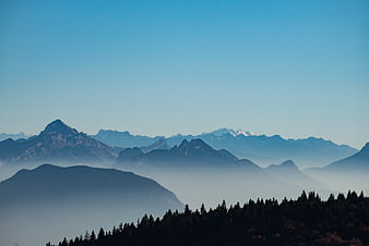 Misty Mountain Range with Forest Silhouette and Blue Sky
