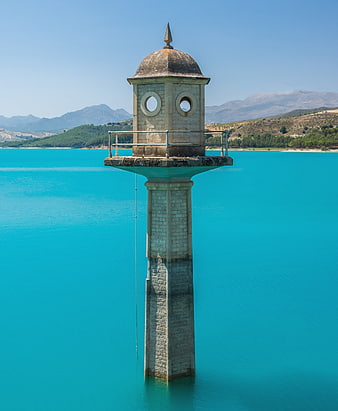Submerged stone watchtower in turquoise reservoir water with mountain backdrop