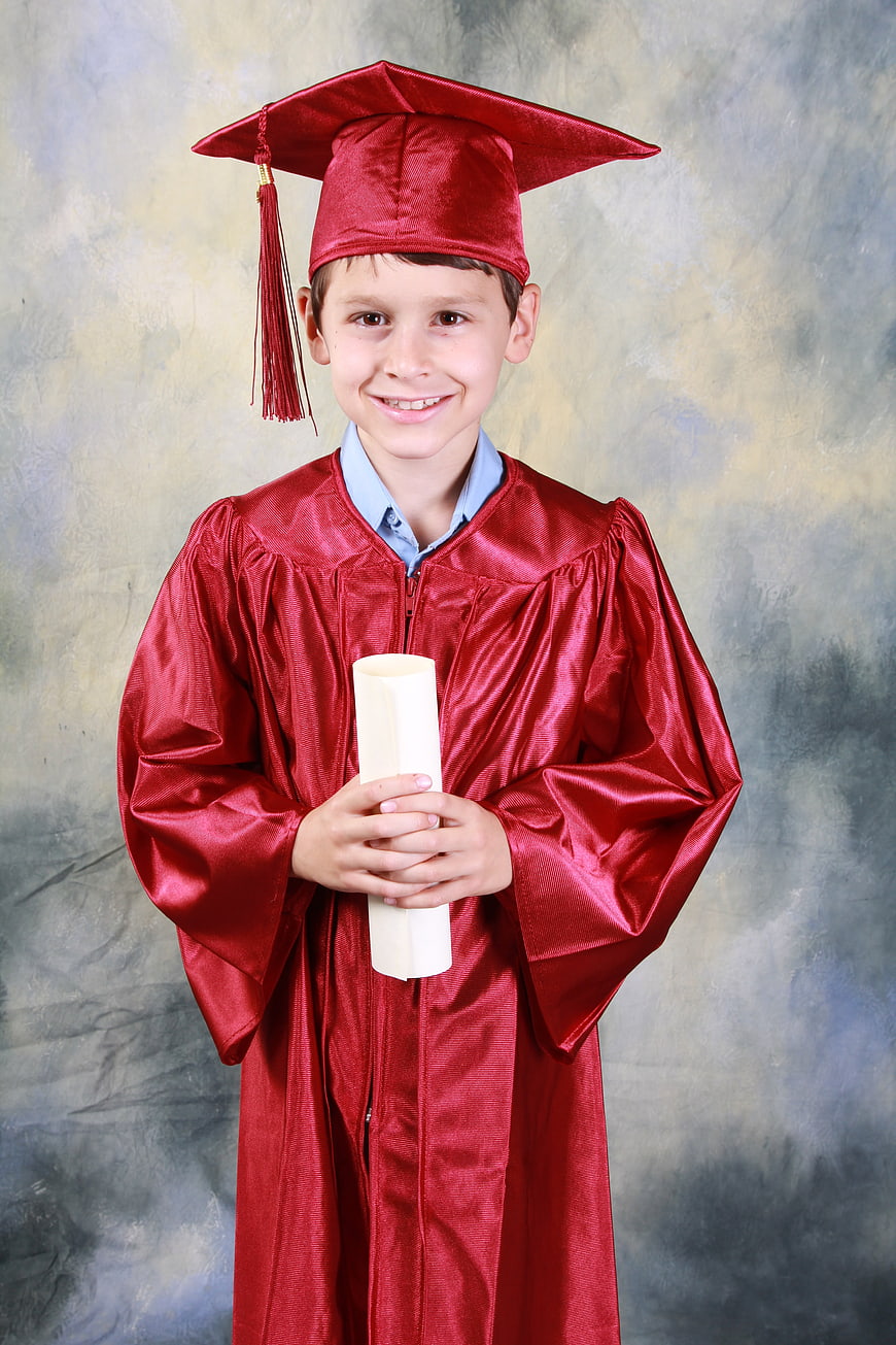 Happy young boy in red graduation gown holding diploma