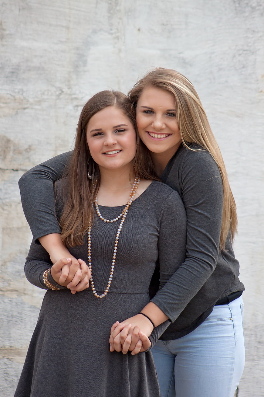 Two smiling young women embracing in front of a textured stone wall