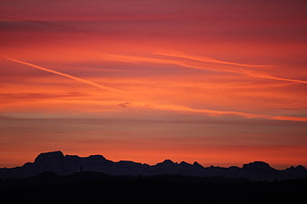 Vibrant orange sunset sky over dark mountain silhouette