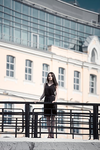 Young woman in black dress standing on bridge railing