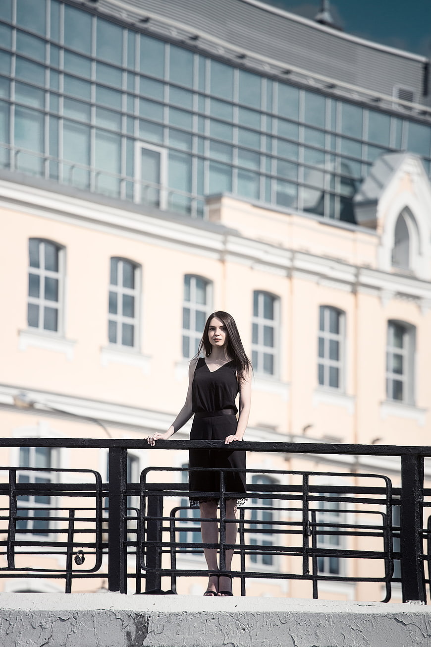 Young woman in black dress standing on bridge railing