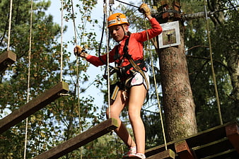 Girl in orange helmet navigating high ropes course obstacle