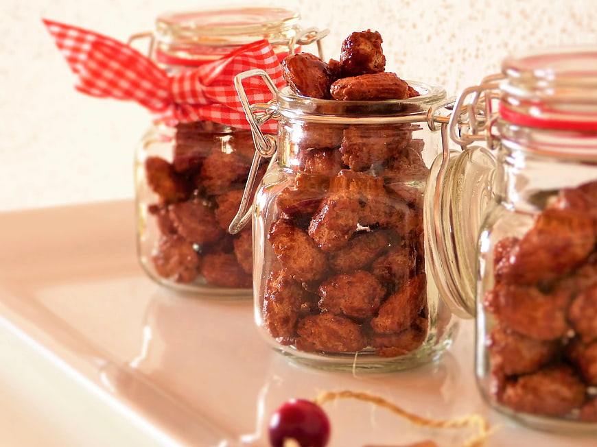 Homemade candied almonds in glass jars on white tray