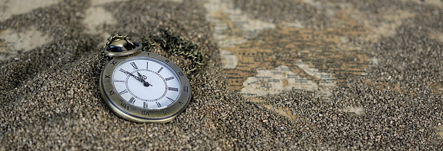 Vintage pocket watch half buried in sand with old map