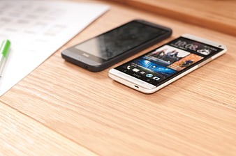 Two smartphones on wooden desk with paper and pen