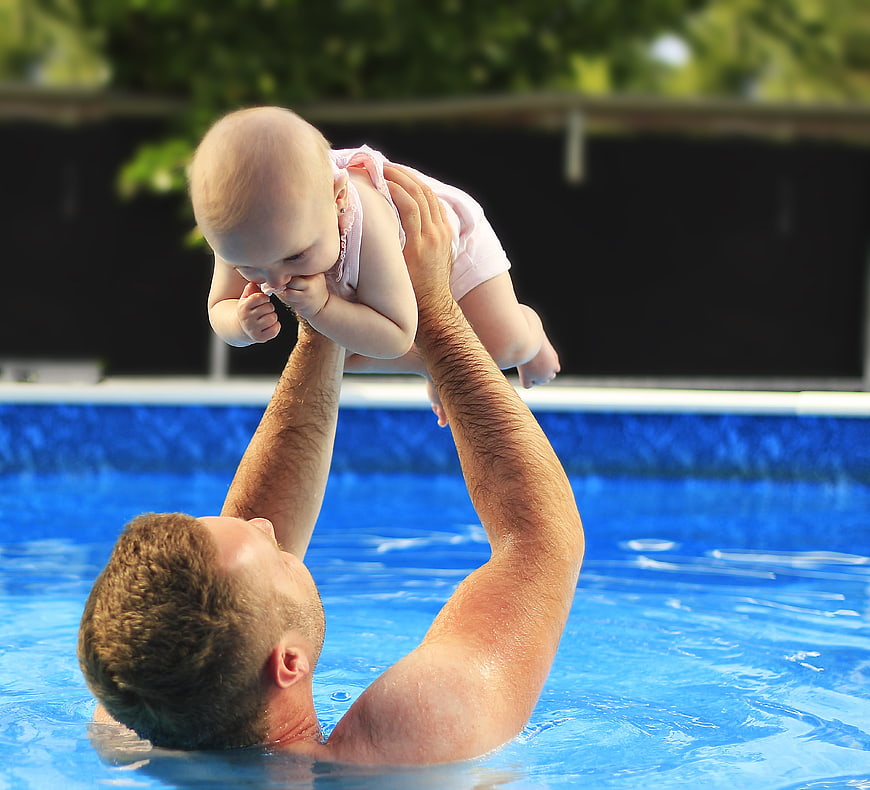 Father lifting baby girl in swimming pool