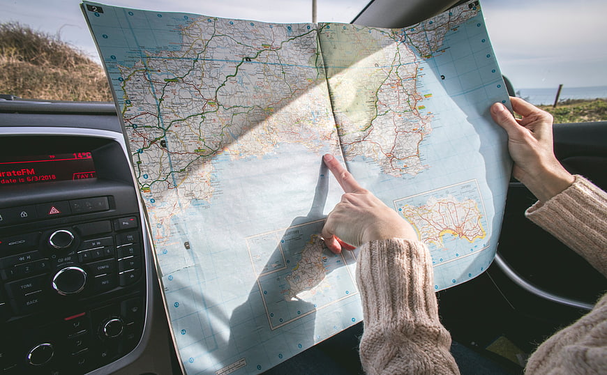 Hands holding paper map inside car during road trip