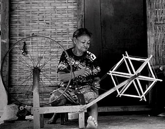 Senior woman spinning yarn on traditional wheel