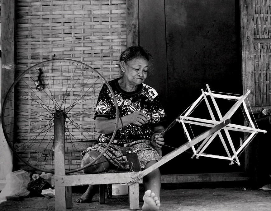 Senior woman spinning yarn on traditional wheel