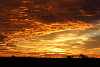 Dramatic fiery orange sunset sky over dark silhouette landscape