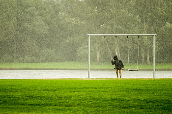 Child swinging alone in heavy rain near a lake