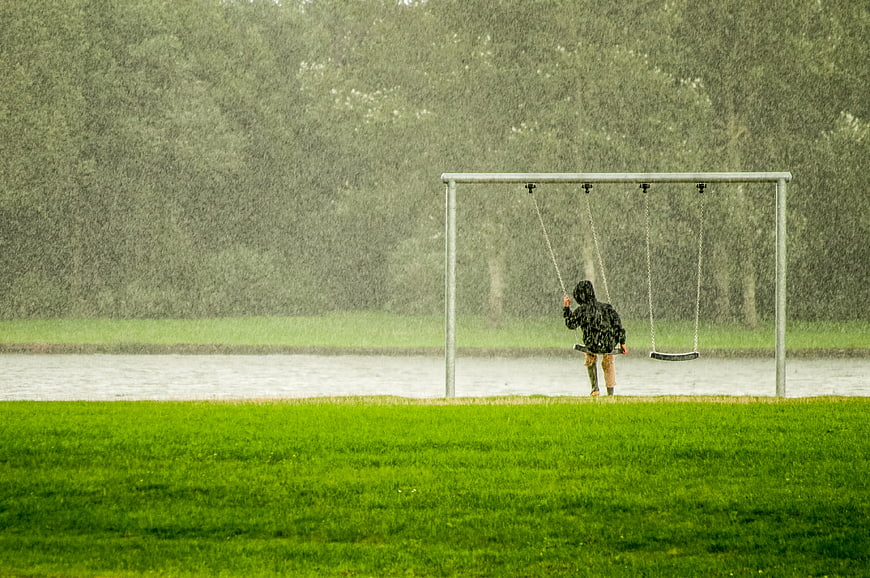 Child swinging alone in heavy rain near a lake