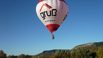 Red and white hot air balloon flying over autumn hills