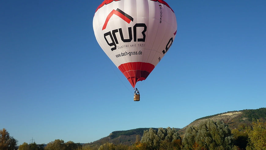 Red and white hot air balloon flying over autumn hills