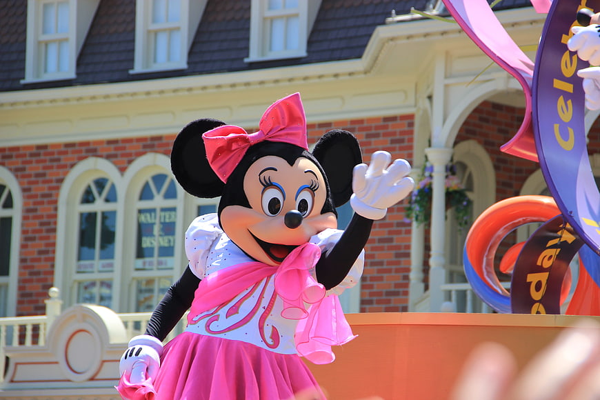 Minnie Mouse waving on a parade float at Disney theme park