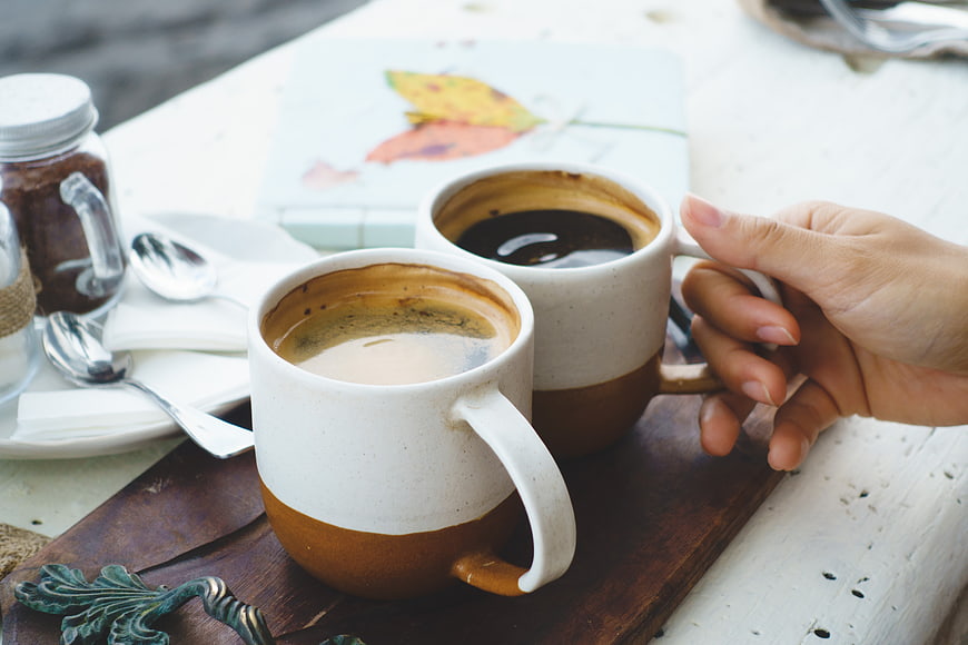 Two ceramic mugs of coffee on a wooden tray outdoors