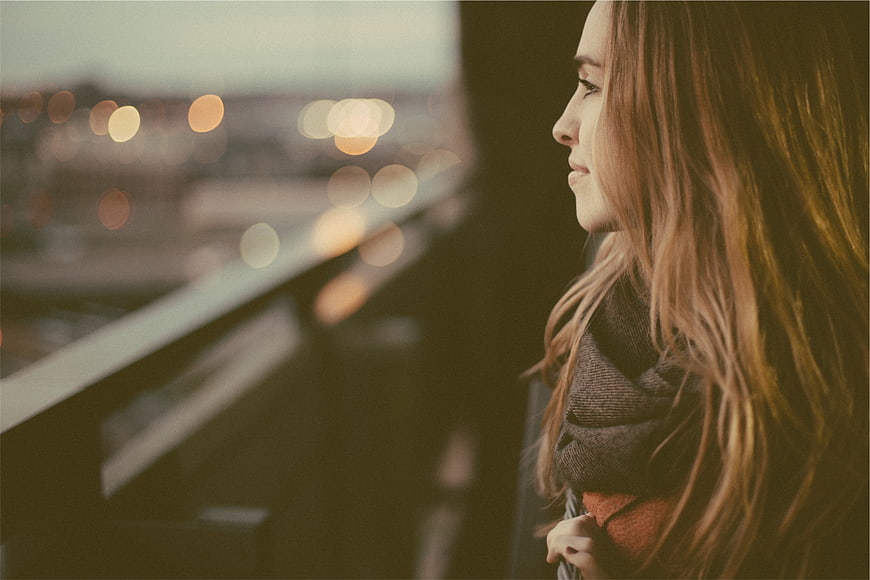 Woman looking out window at city lights at dusk