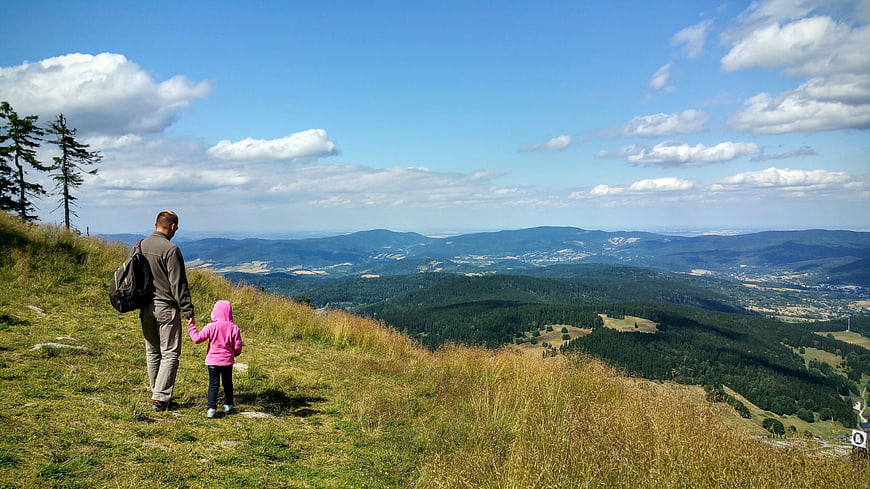 Father and daughter holding hands on a grassy mountain ridge overlooking a vast valley