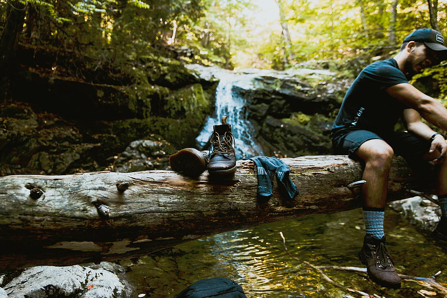 Hiker resting by forest waterfall with boots on log