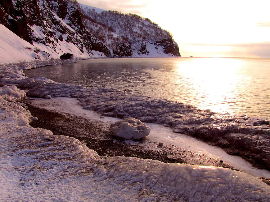 Frozen Winter Beach Landscape with Snowy Cliffs and Sunset