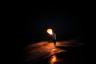 Person Releasing Glowing Sky Lantern on Dark Beach at Night