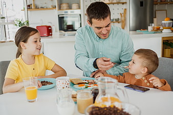 Father feeding toddler breakfast with daughter in kitchen