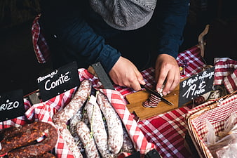 Butcher slicing cured sausage at a rustic market stall