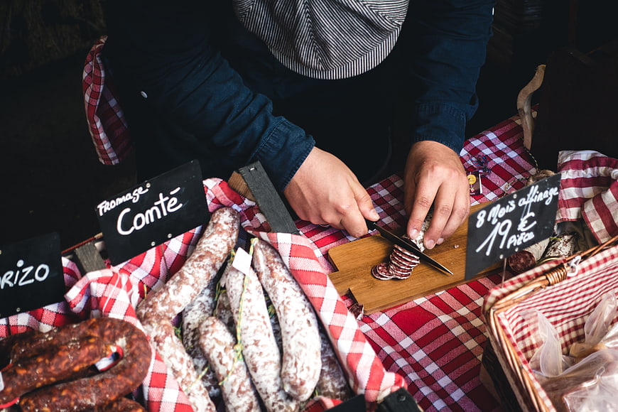 Butcher slicing cured sausage at a rustic market stall