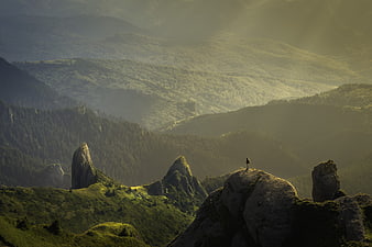 Lone Hiker Standing on Rocky Mountain Peak in Misty Green Valley