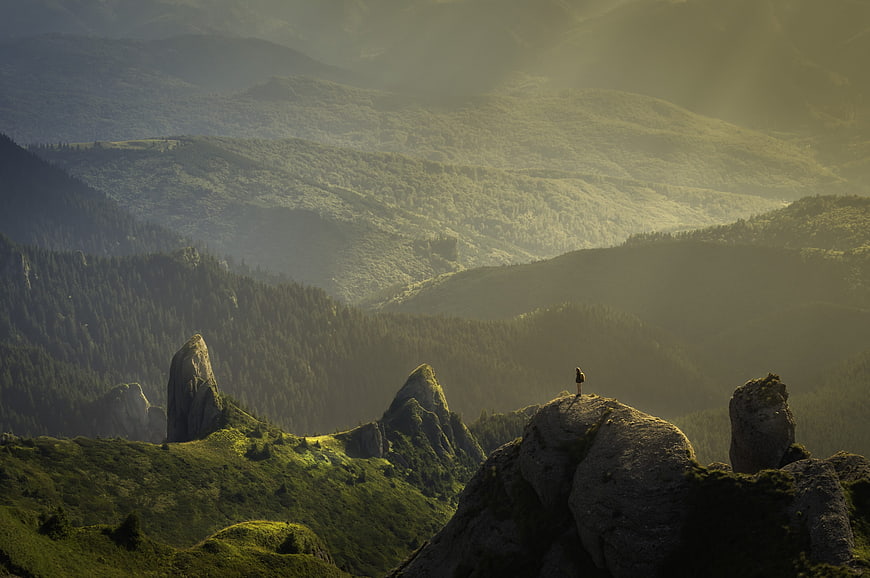 Lone Hiker Standing on Rocky Mountain Peak in Misty Green Valley