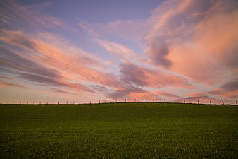 Vibrant pink and purple sunset clouds over green meadow
