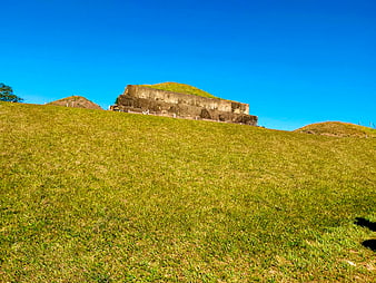 Ancient Mayan pyramid ruins on grassy hill under blue sky