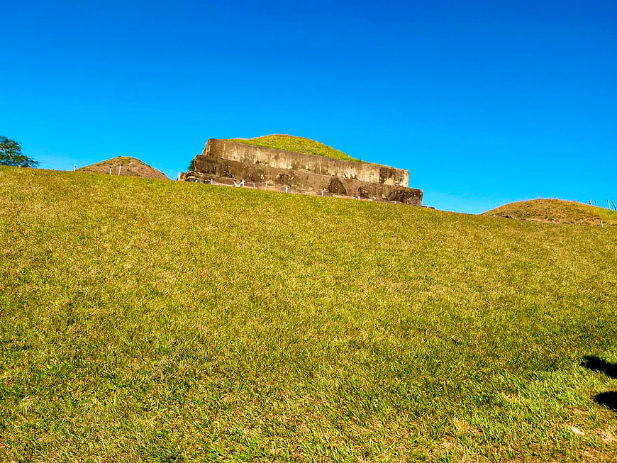 Ancient Mayan pyramid ruins on grassy hill under blue sky