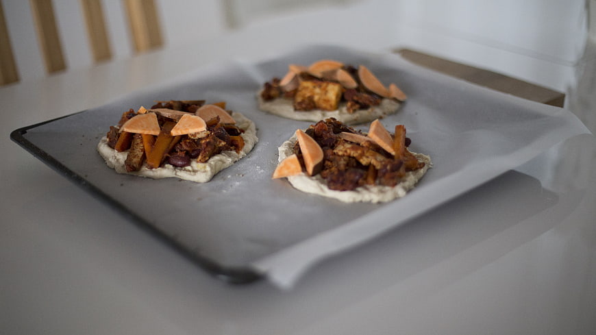 Unbaked mini pizzas with sweet potato and beans on baking sheet