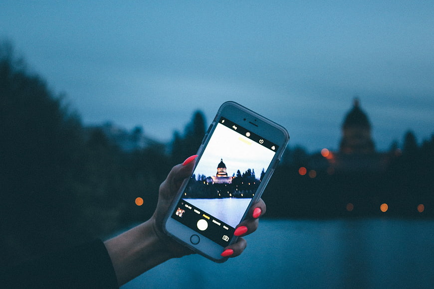 Hand holding smartphone taking photo of cityscape at dusk