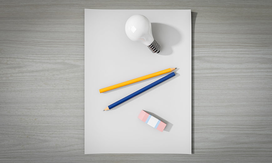 Top view of light bulb, pencils, and eraser on white paper