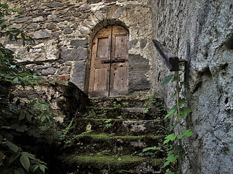 Mossy Stone Steps Leading To Weathered Wooden Door In Old Stone Wall